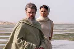 A gray-bearded Odysseus standing next to Athena on a beach.