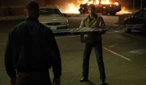 Hal Jordan (Kyle Chandler) holds out a satelite to John Stewart (Aaron Pierre) as a pickup truck burns in the background in Lanterns