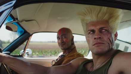 Guile with a slash on his face looking out the window of his car, with Dhalsim in the background.