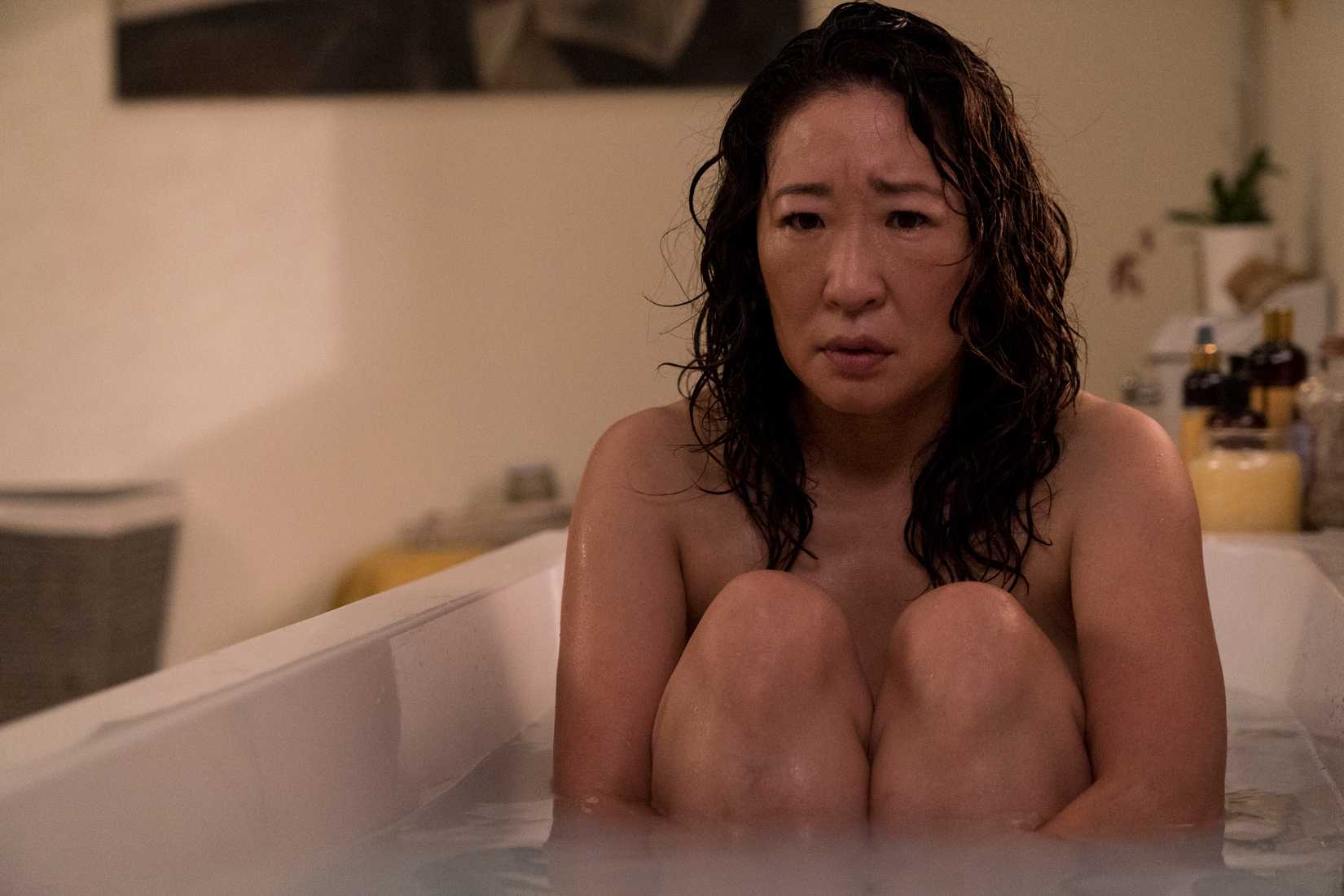 Sandra Oh sits in a bathtub looking miserable, knees drawn up to her chest, in Killing Eve