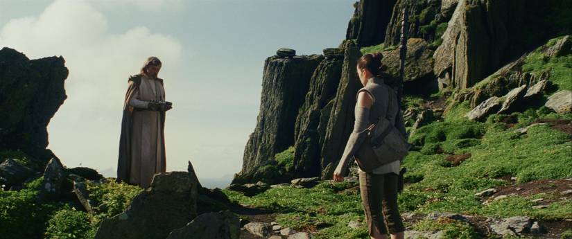 Rey looks at Luke holding his lightsaber on Ahch-To in Star Wars: The Last Jedi