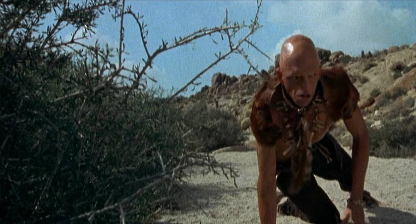 Pluto (Michael Berryman) crouches behind a bush in a still from The Hills Have Eyes