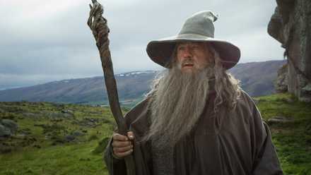 Gandalf the Grey holding his staff with a verdant, hilly field behind him in The Hobbit: An Unexpected Journey