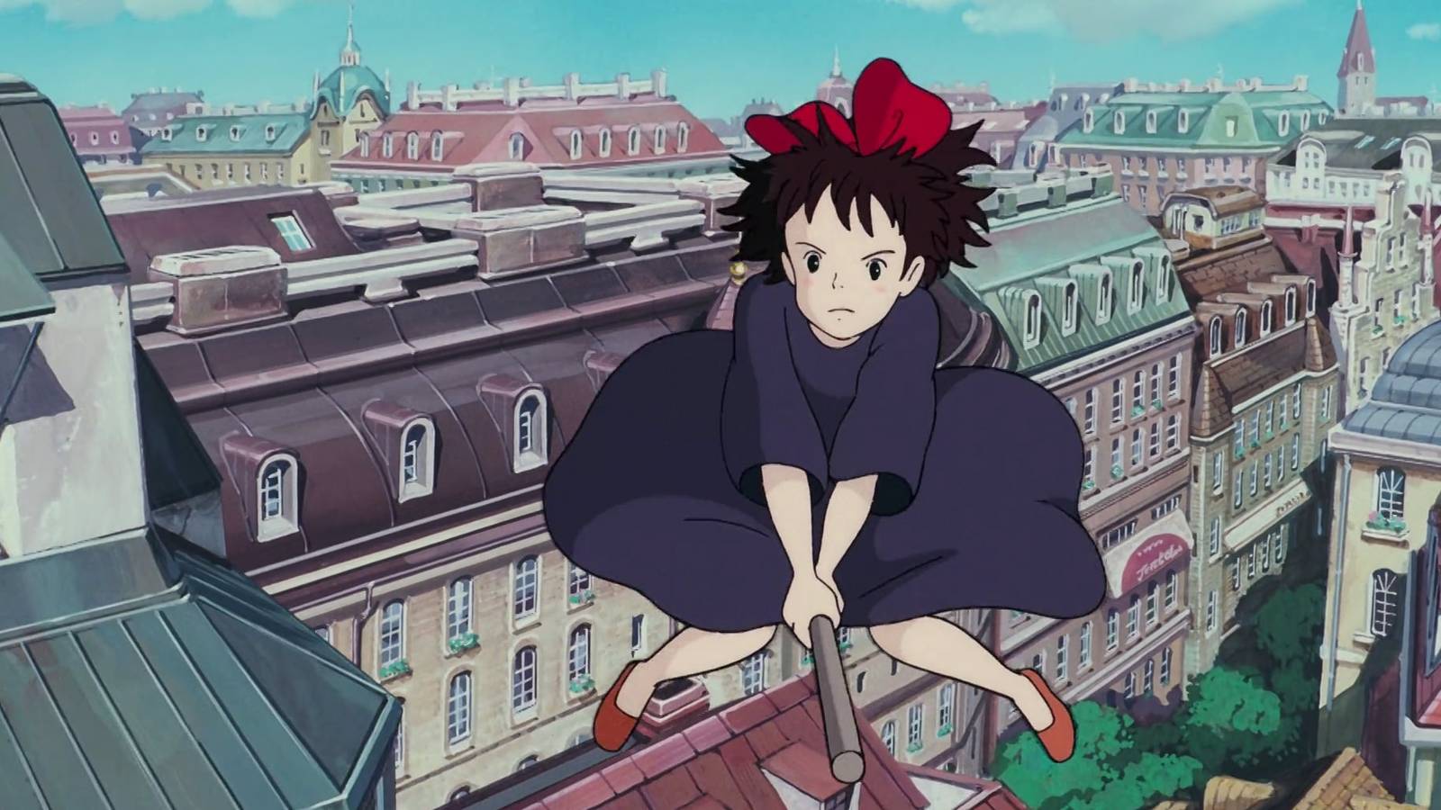 Kiki, an anime girl with black hair and a red bow on top, rides a broom over a European-style cityscape in Studio Ghibli’s Kiki’s Delivery Service.