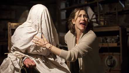 Lorraine Warren (Vera Farmiga), looking distressed, touches a woman covered in a sheet in the first Conjuring movie.