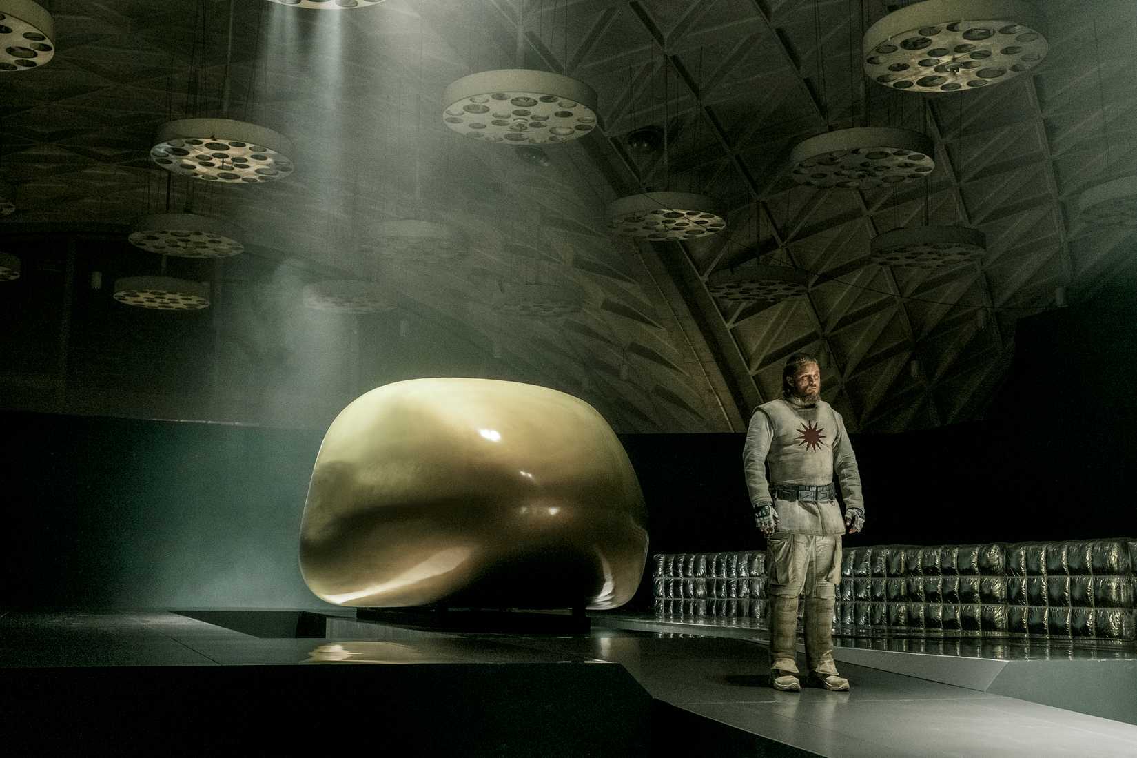 Travis Fimmel stands by a sleek, shiny space-pod in a weird space-hangar in Raised By Wolves.