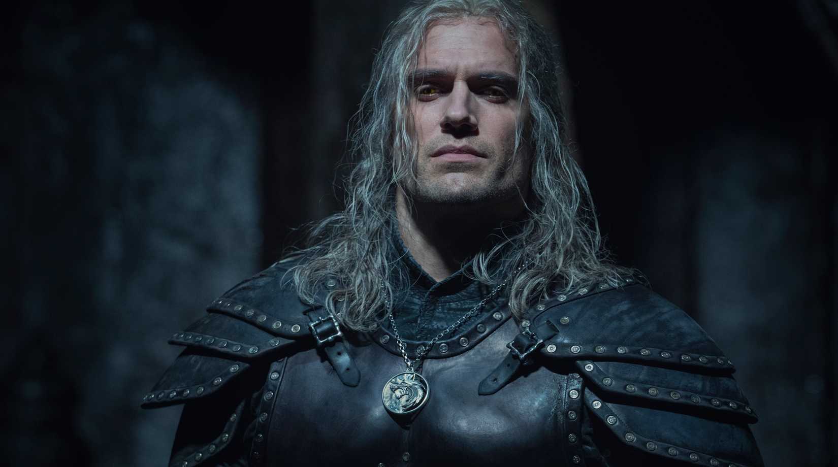 Henry Cavill in The Witcher season 2 cropped at his bulky chest wearing giant studded armor and a wolf medallion, his white hair looking extra crinkled