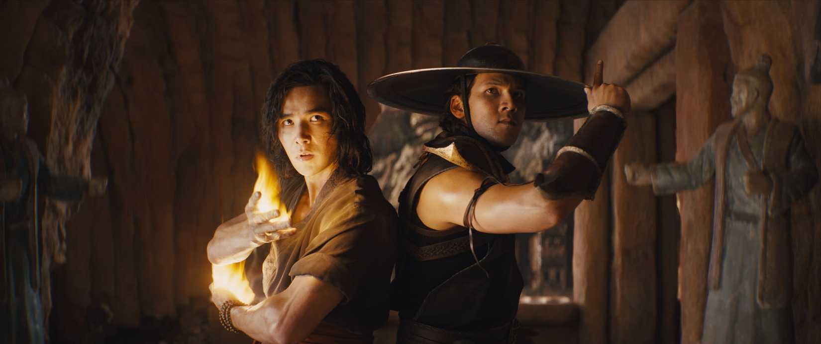 Liu Kang (Ludi Lin), with flames in his hand, and Kung Lao (Max Huang), wearing a wide-brimmed metal hat with a serrated saw edge, stand back to back in Mortal Kombat (2021)