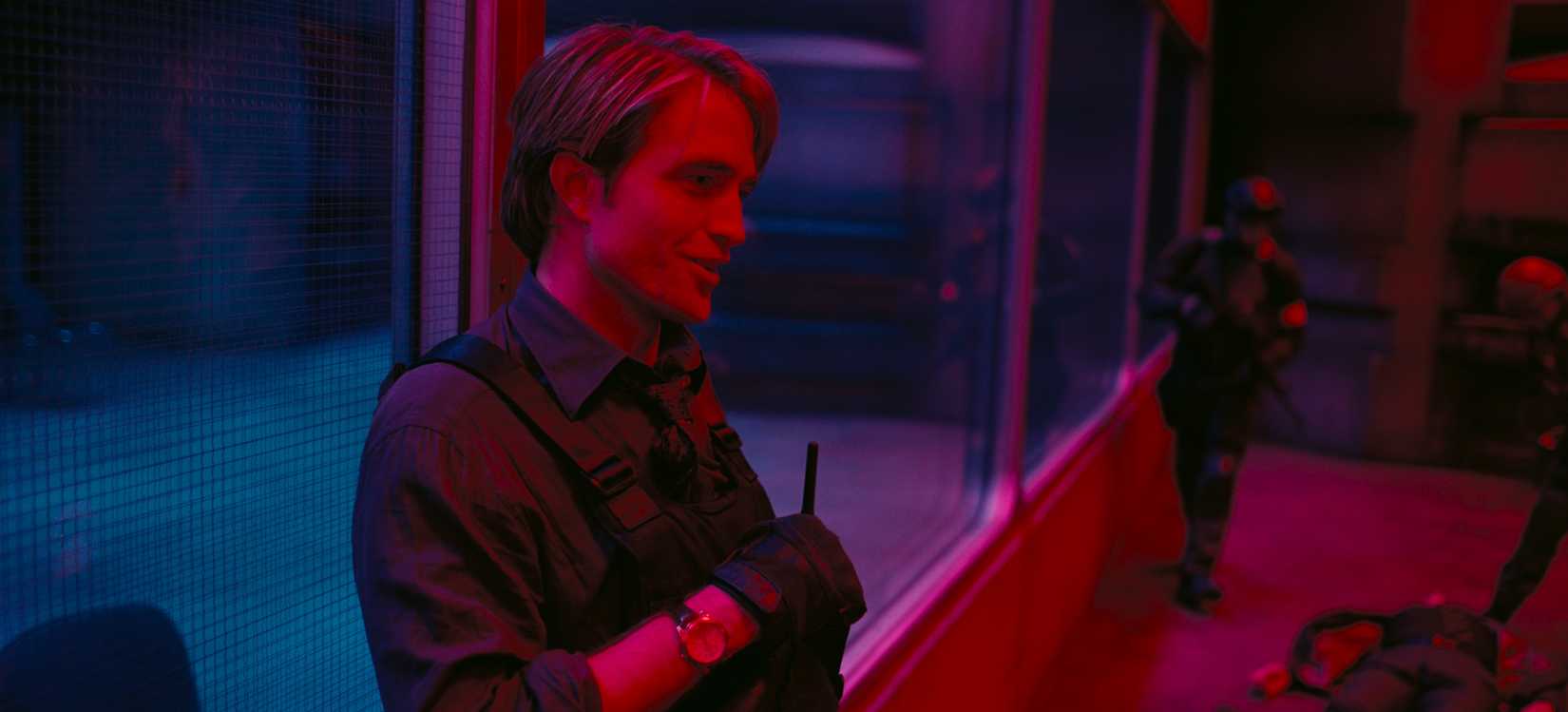 Robert Pattinson wearing a bullet-proof vest as Neil in Tenet washed with red and blue light