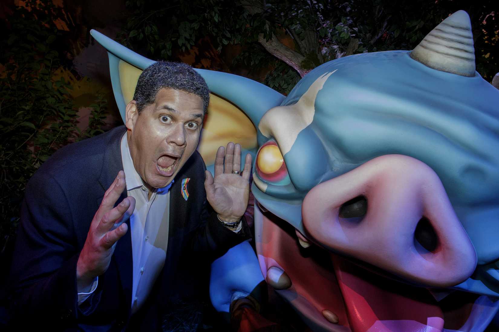 Reggie Fils-Aime makes a funny face next to an oversized statue of a bokoblin, a cartoony creature from the Legend of Zelda