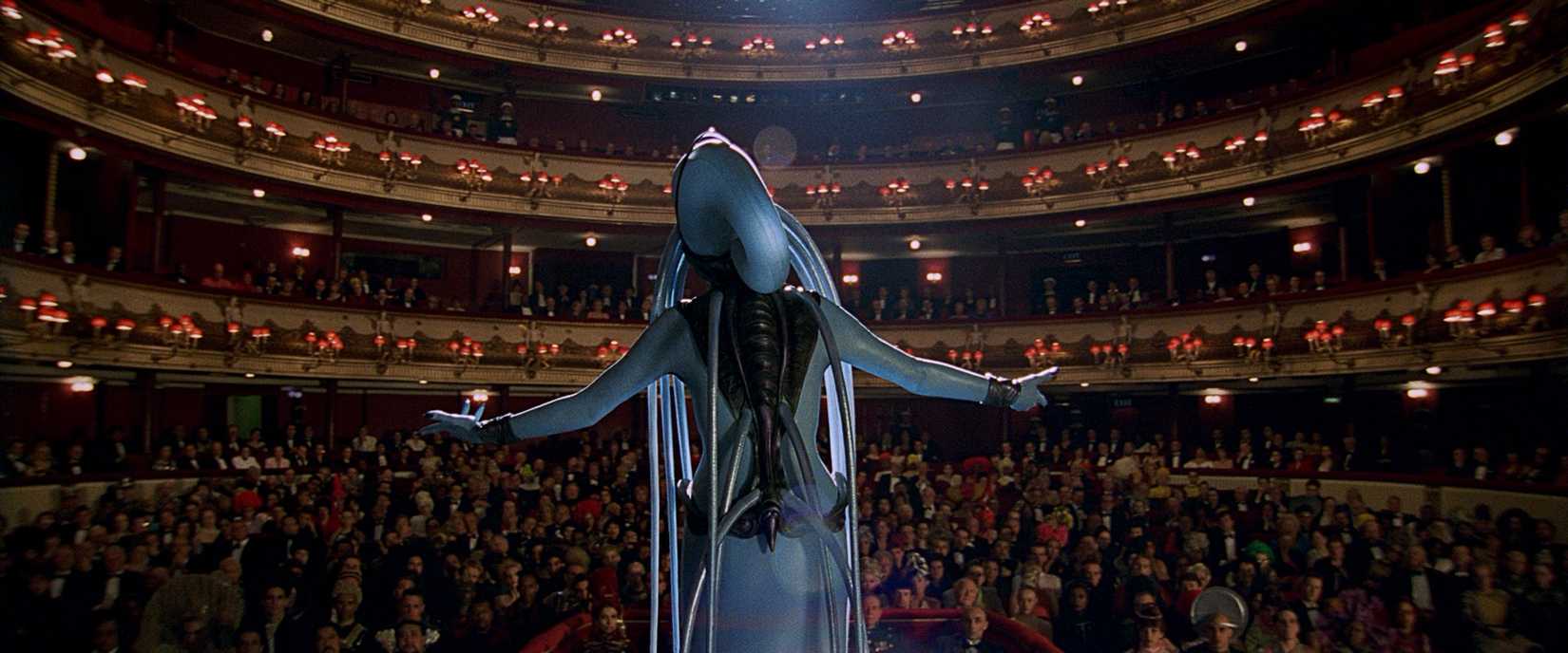 A cantora de ópera alienígena de pele azul, vista por trás, cantando para uma casa de ópera lotada no quinto elemento