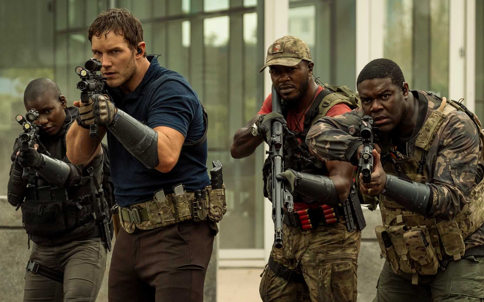 Chris Pratt stands meaningfully at the head of a small group of armed and camo-wearing soldiers, all of whom are Black except him