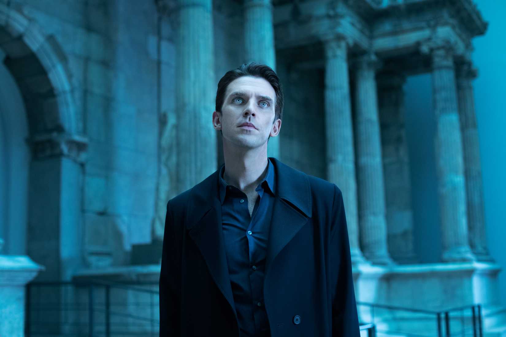 Dan Stevens, as the AI Tom in I’m Your Man, stands in a blue-lit columned ampitheater, looking upward