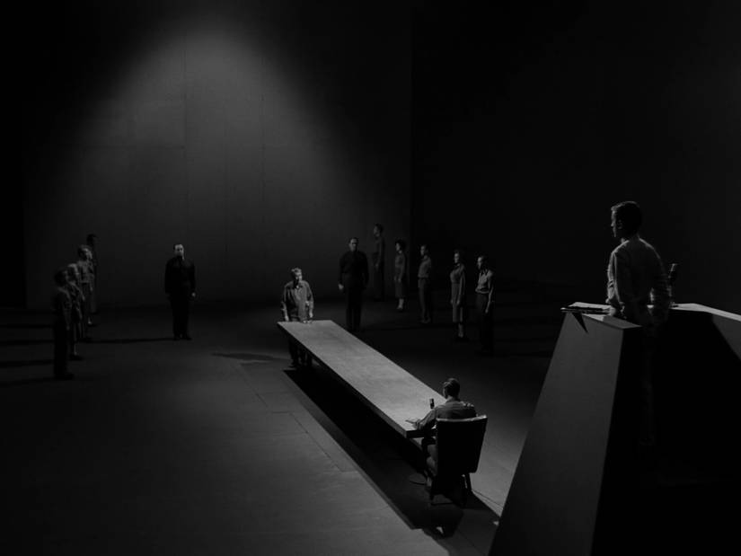 A man stands at the far end of a table awaiting trial in The Twilight Zone episode “The Obsolete Man.”