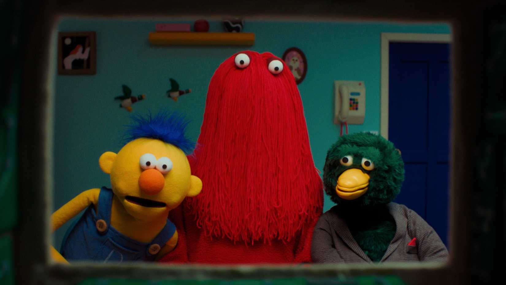 Yellow Guy, Red Guy and Duck from Don’t Hug Me I’m Scared staring through the frame of a television.