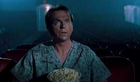 Sam Neill, sitting in a movie theater alone with a tub of popcorn, gapes at the screen in awe in the movie In the Mouth of Madness
