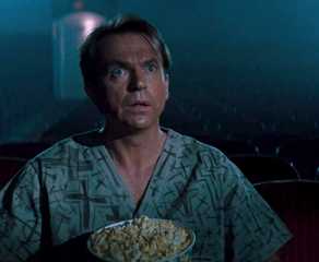 Sam Neill, sitting in a movie theater alone with a tub of popcorn, gapes at the screen in awe in the movie In the Mouth of Madness