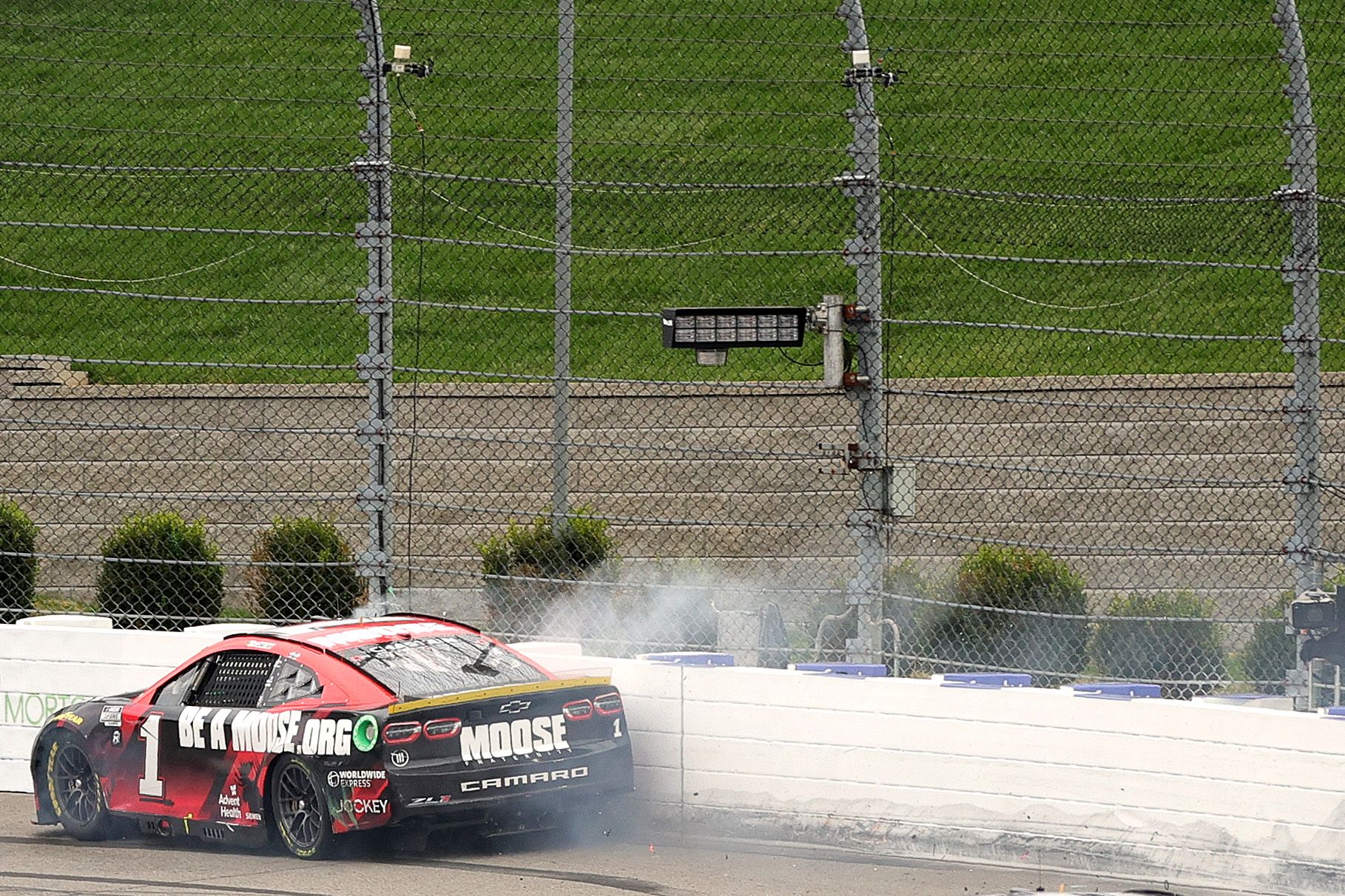 Stock car No. 1, headed right to left, hugs the white concrete barrier ringing Martinsville Speedway, with a cloud of debris and paint trailing off the side