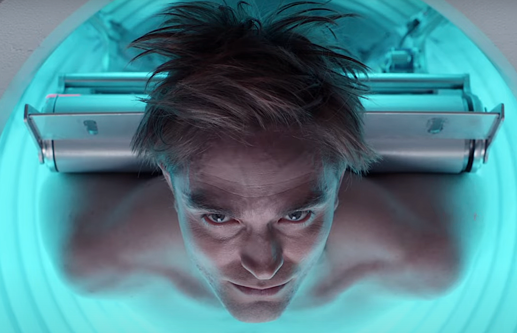 Robert Pattinson lies on his back, shirtless, in a glowing blue MRI-type machine, staring directly into the camera, in an early teaser trailer for Bong Joon-ho’s Mickey 17