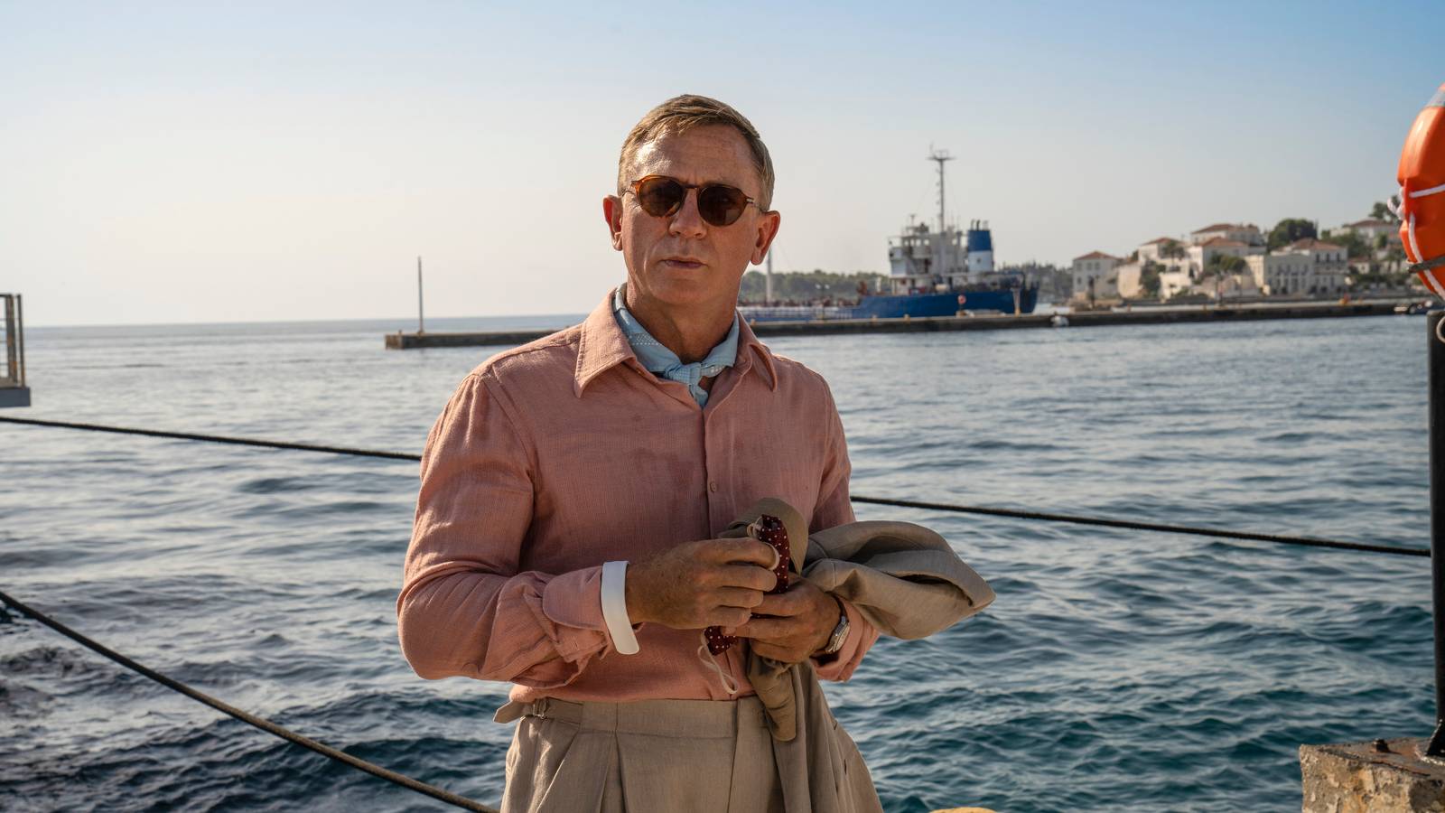 Daniel Craig wears a salmon top by the water in Glass Onion.