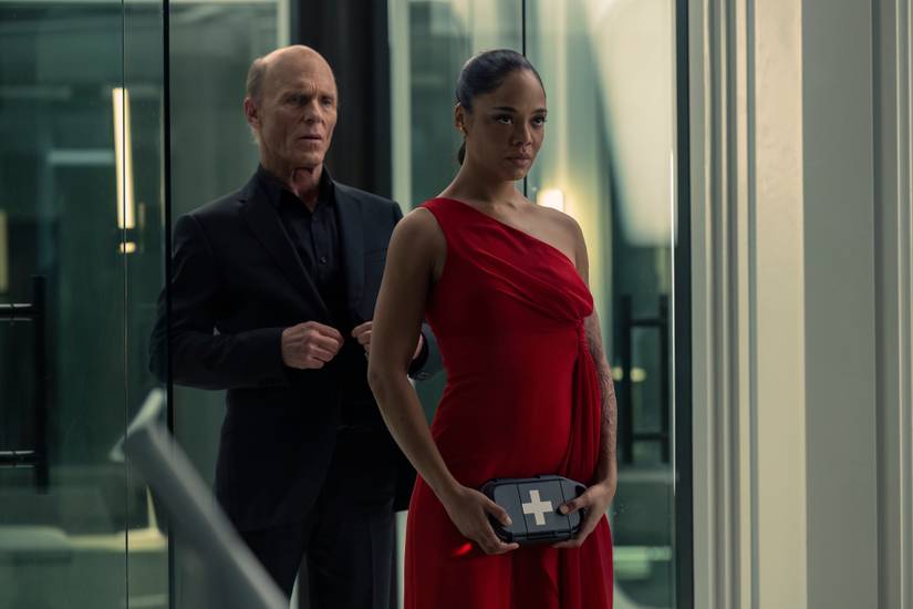 A robo version of the Man in Black (Ed Harris) stnads behind Charlotte Hale (Tessa Thompson) in a silky red dress, holding a device in her hand, which is affected by some kind of skin issue