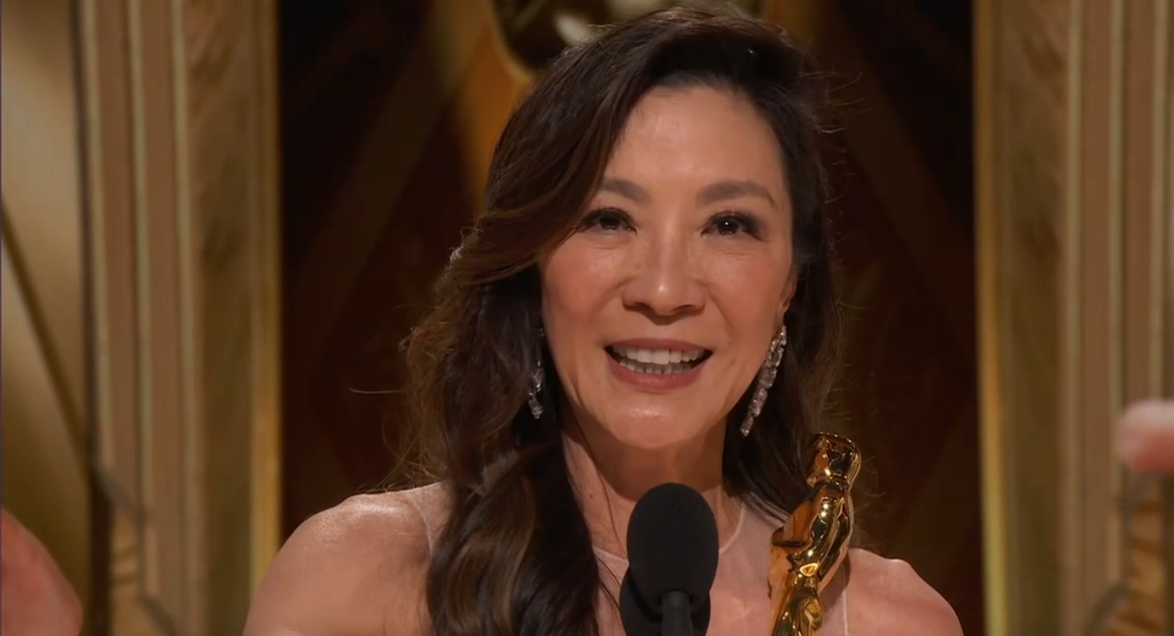 Michelle Yeoh smiling as she holds her Oscar while giving her speech