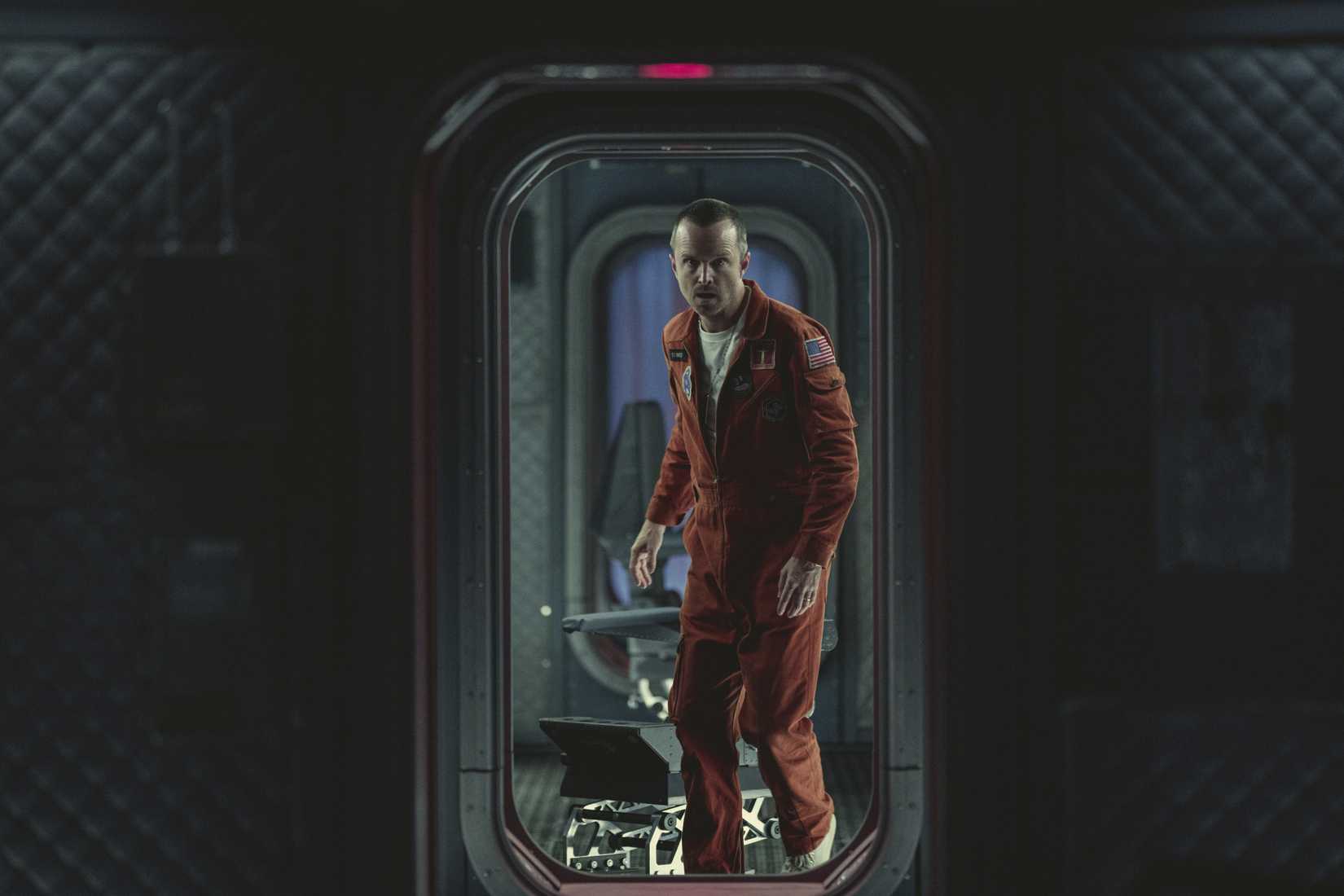 Aaron Paul in a spacesuit looking through a doorway with shock in a still from Black Mirror season 6