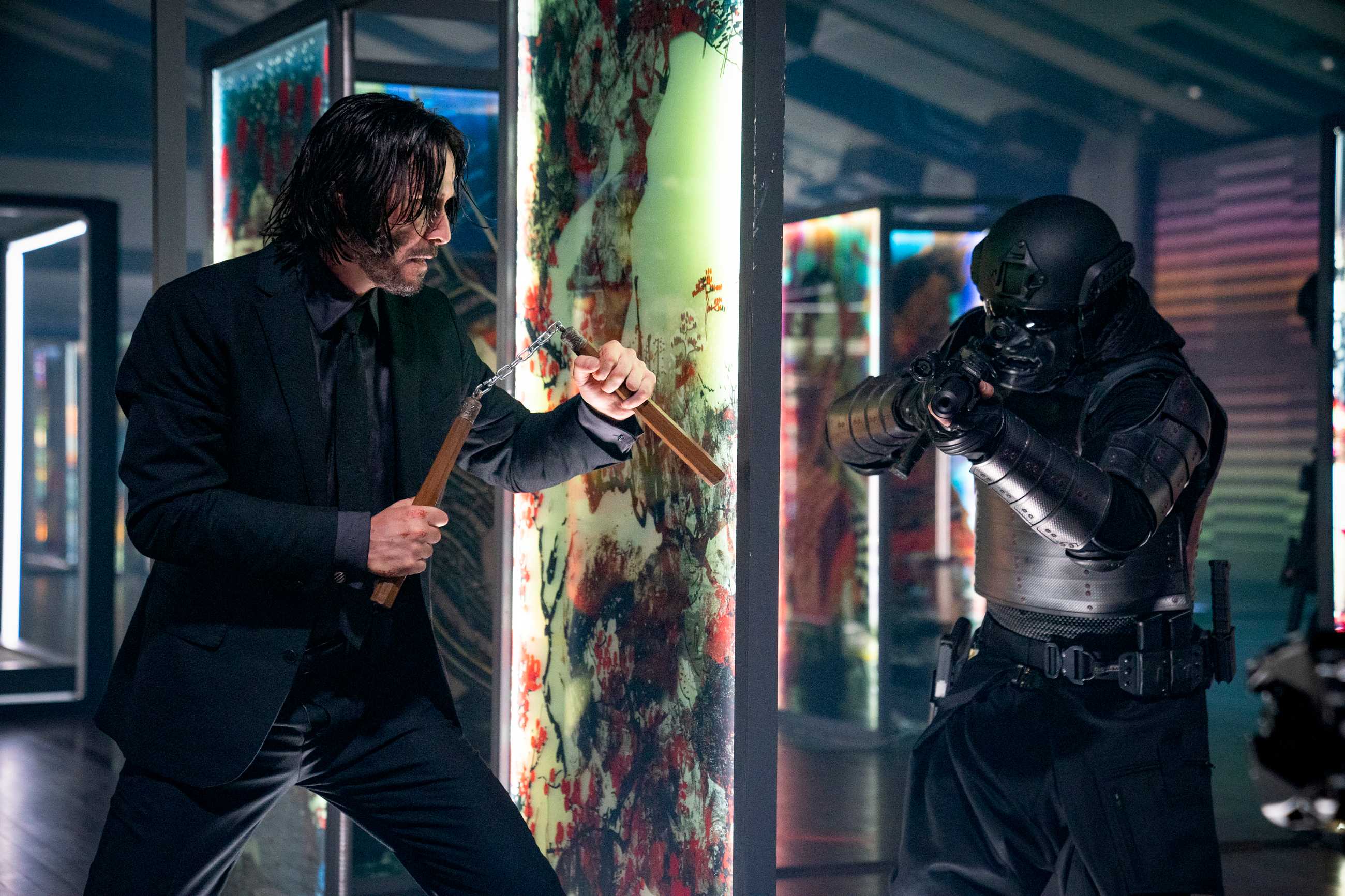 Keanu Reeves as John Wick holding num-chuks behind a glass panel preparing to ambush a soldier in black samurai armor in