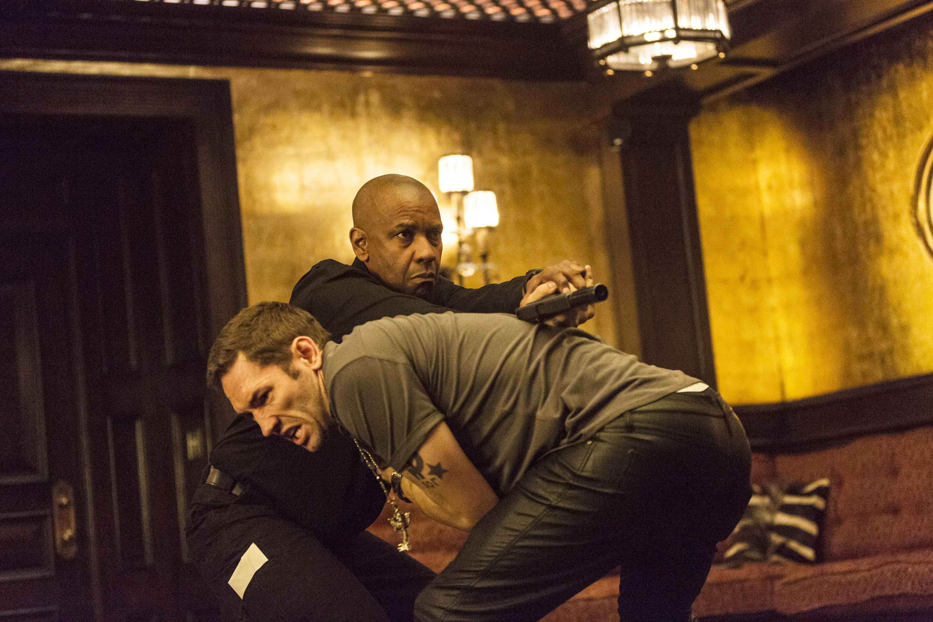 Denzel Washington twists a man’s arm behind his back while holding a gun in The Equalizer.