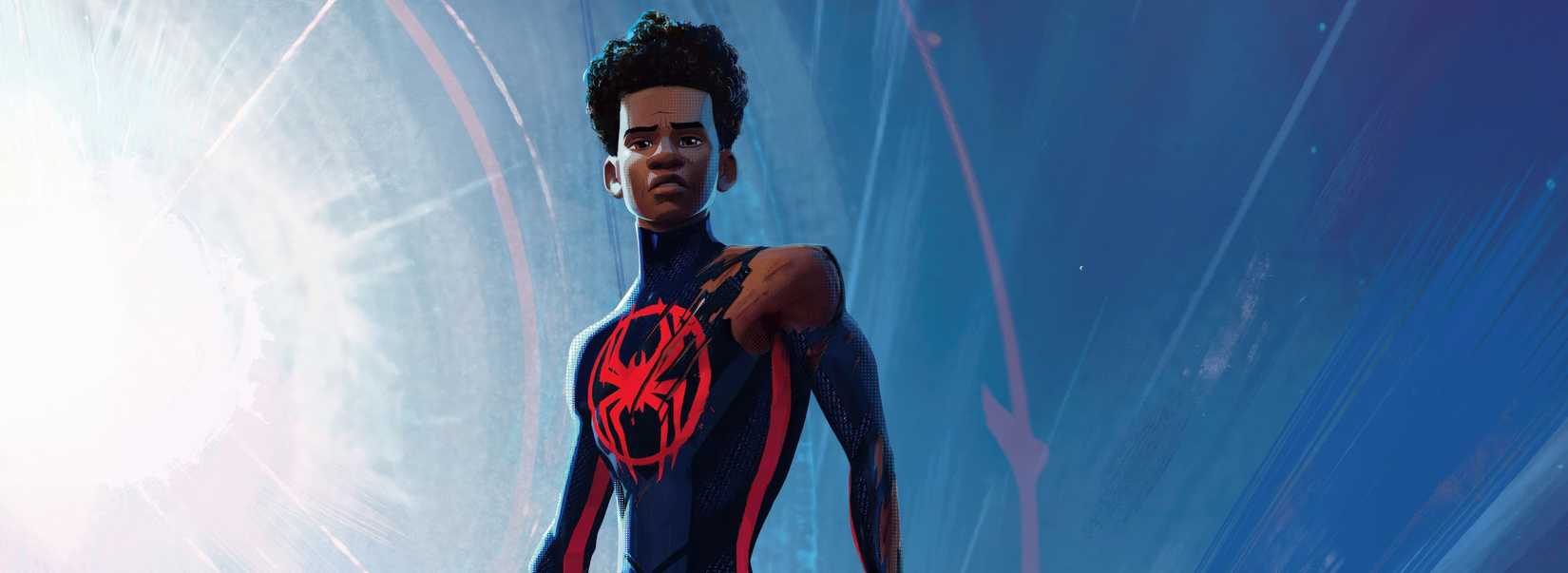 Miles Morales in his dark-hued Spider-Man costume, stands unmasked, the shoulder of his costume torn off, looking down as a huge lens flare lights up the sky behind him in Across the Spider-Verse 