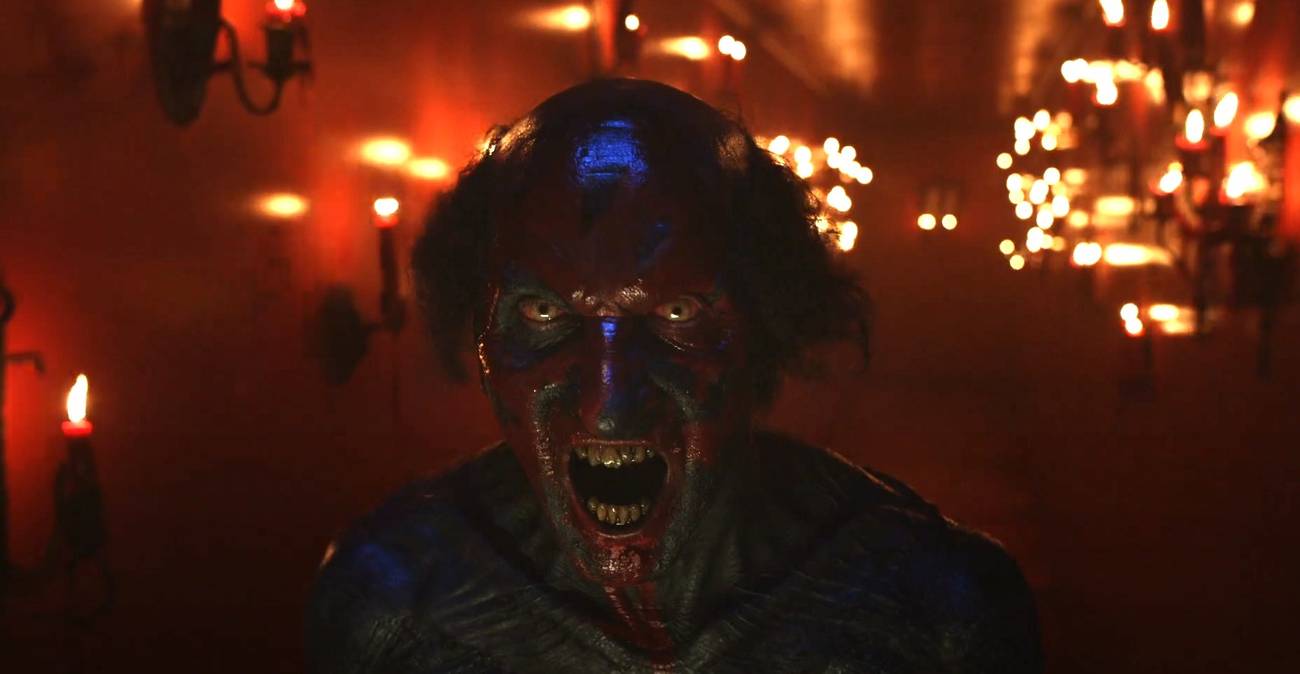 Joseph Bishara as a black and red-faced demon screaming in a hallway filled with lit candles in Insidious: The Red Door.