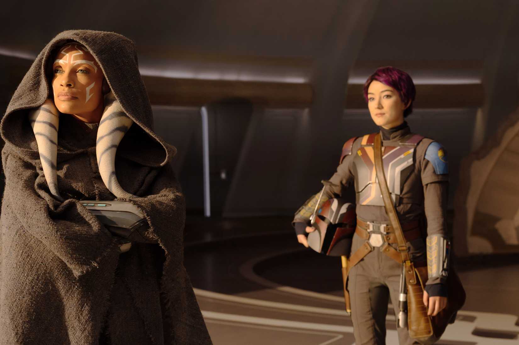 Ahsoka (Rosario Dawson) standing and looking out at something while Sabine (Natasha Liu Bordizzo) stands behind her in her Mandalorian gear