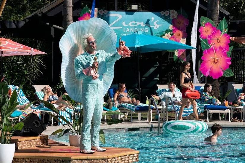 Walton Goggins wears a bright blue outfit with a fabric shell behind him as he sings by the pool in The Righteous Gemstones.