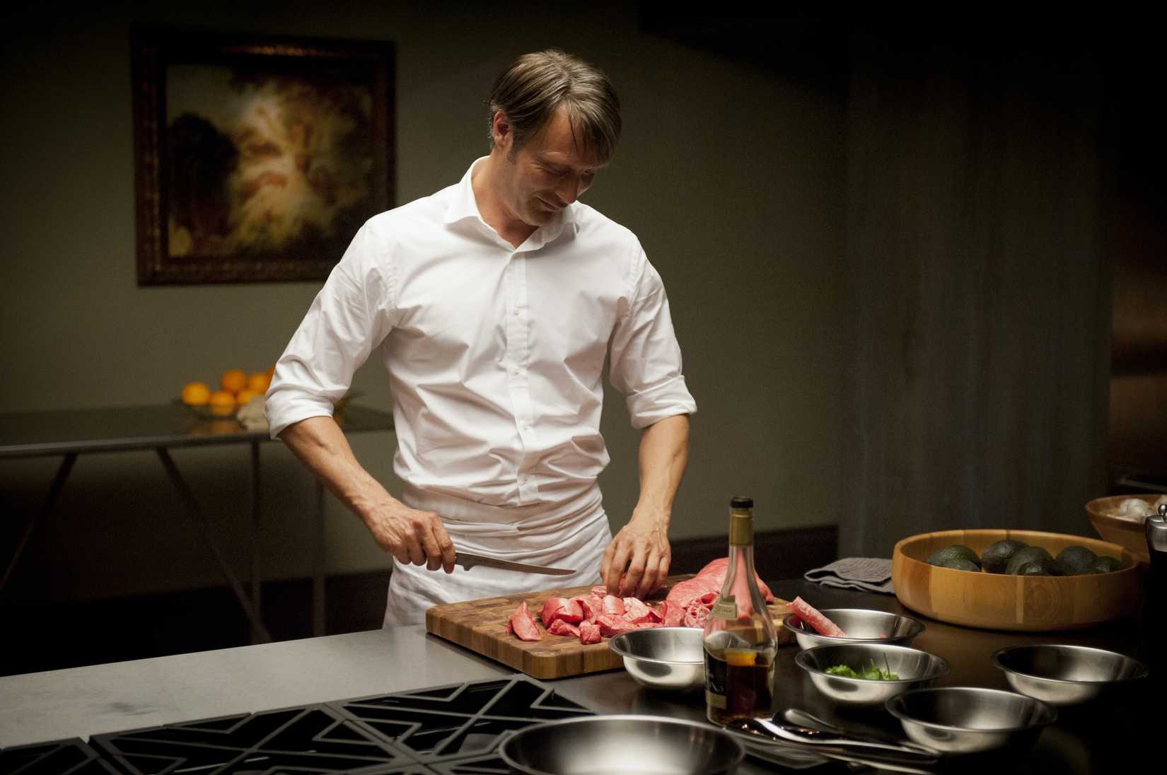 Hannibal (Mads Mikkelsen) chops some meat of dubious origin in Hannibal