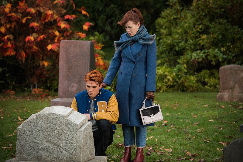 Archie (KJ Apa) kneeling in front of a grave while his mom puts her hand on his shoulder