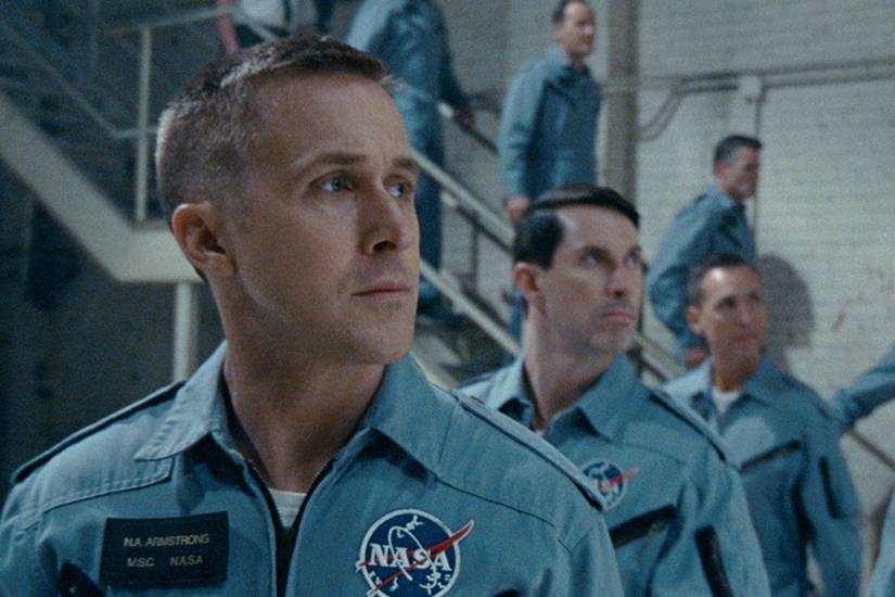 Ryan Gosling as Neil Armstrong standing next to his fellow astronauts in a blue uniform in First Man.