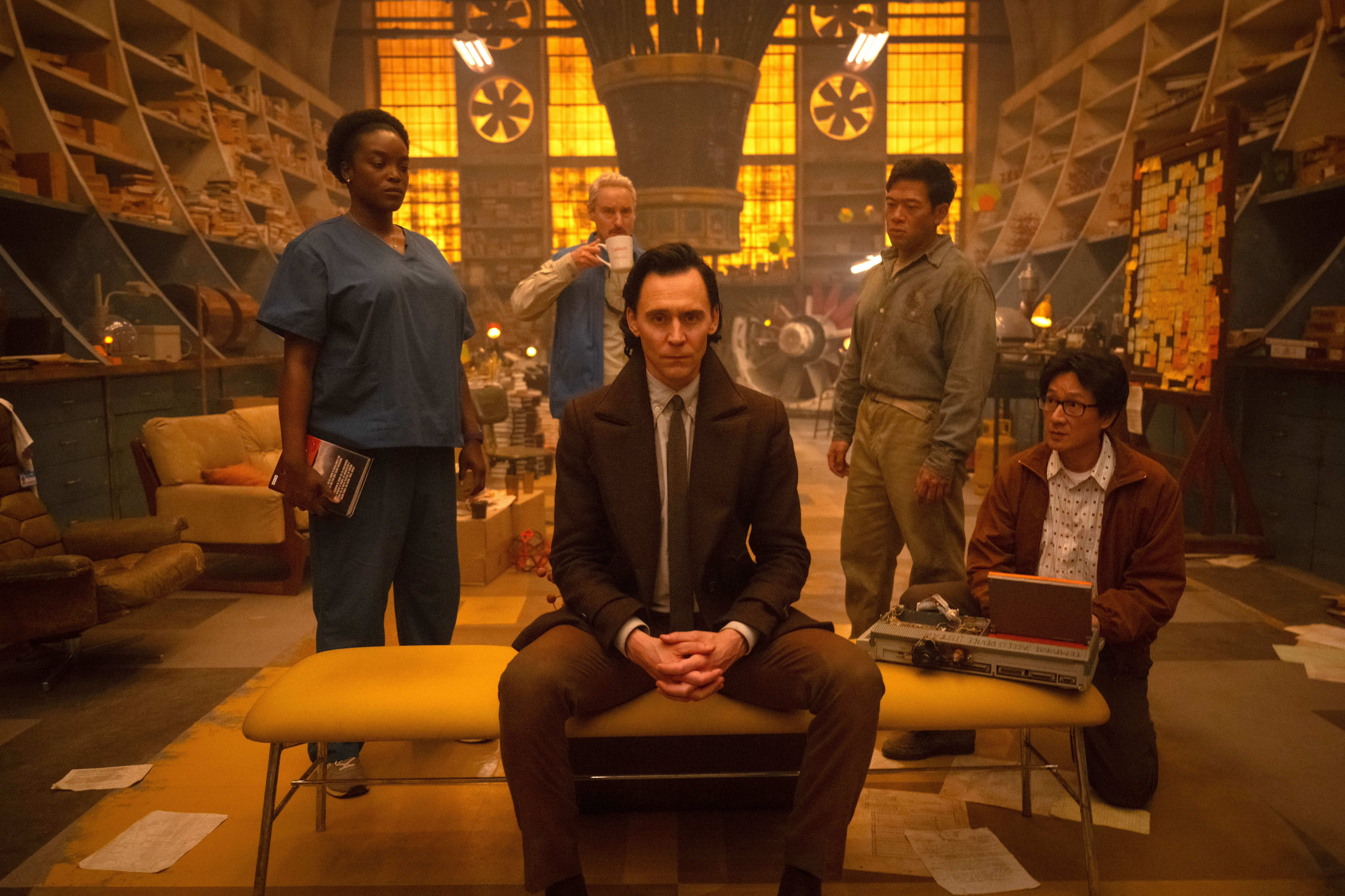 Loki (Tom Hiddleston) đang ngồi và tỏ ra lo lắng với các thành viên của TVA phía sau