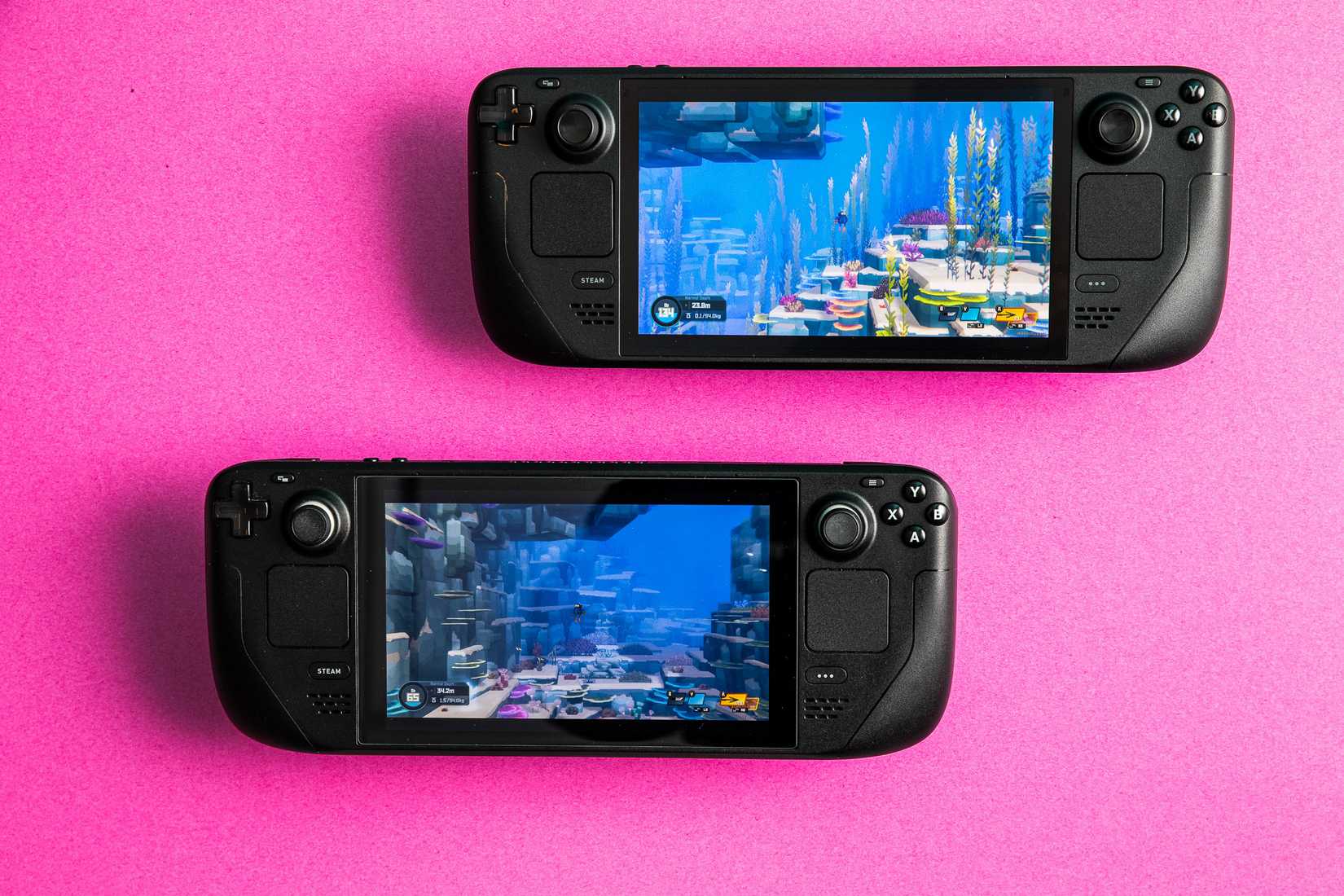 a photo of the Steam Deck OLED (top) and the original Steam Deck, lying on a hot pink sheet of thick paper, with Dave the Diver running on both handhelds