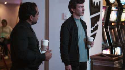 Asher (Nathan Fielder) stands looking at something in quiet disbelief while someone talks to him