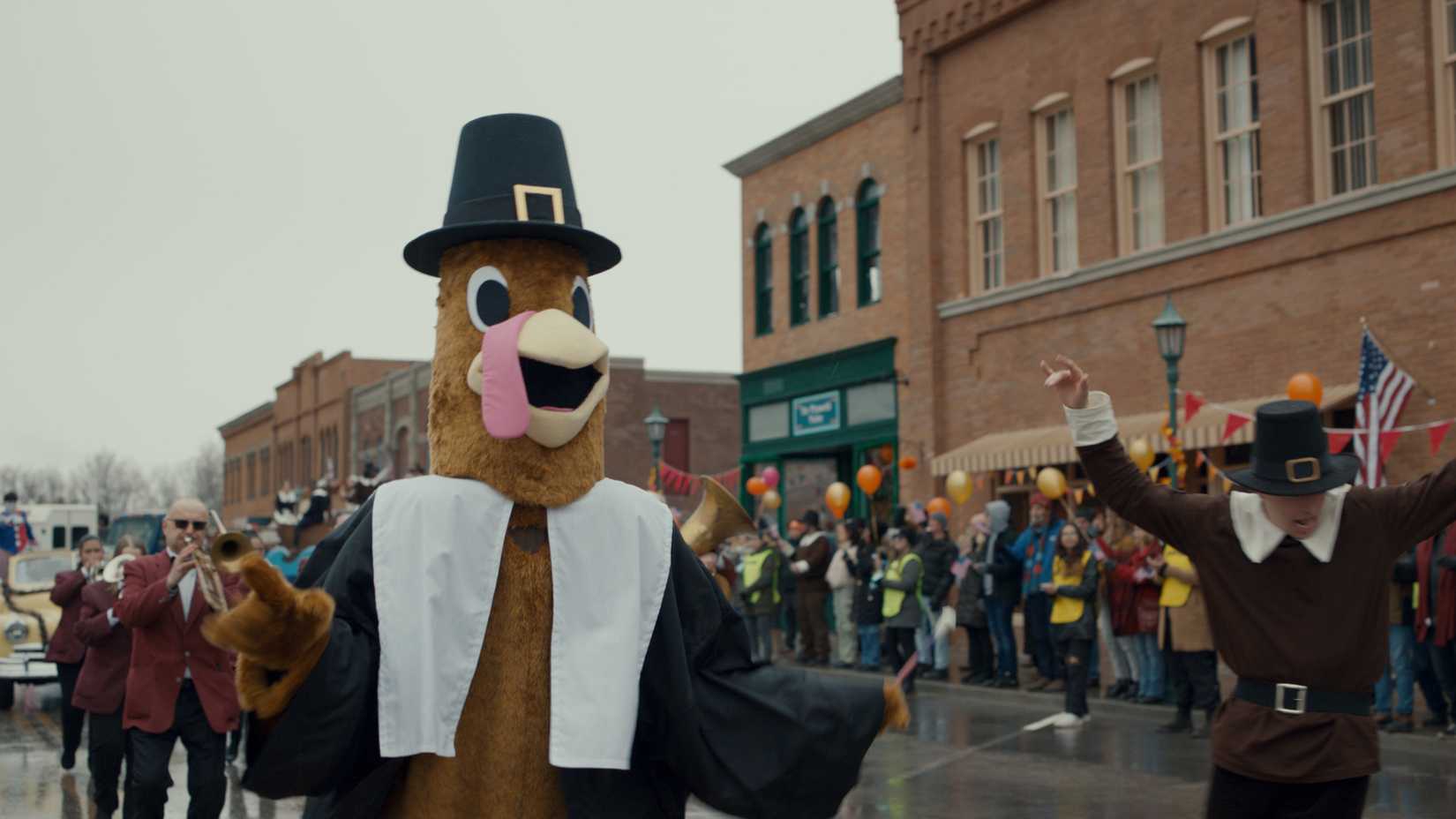 A person in a turkey suit walks down the street in a Thanksgiving Day parade in the movie Thanksgiving