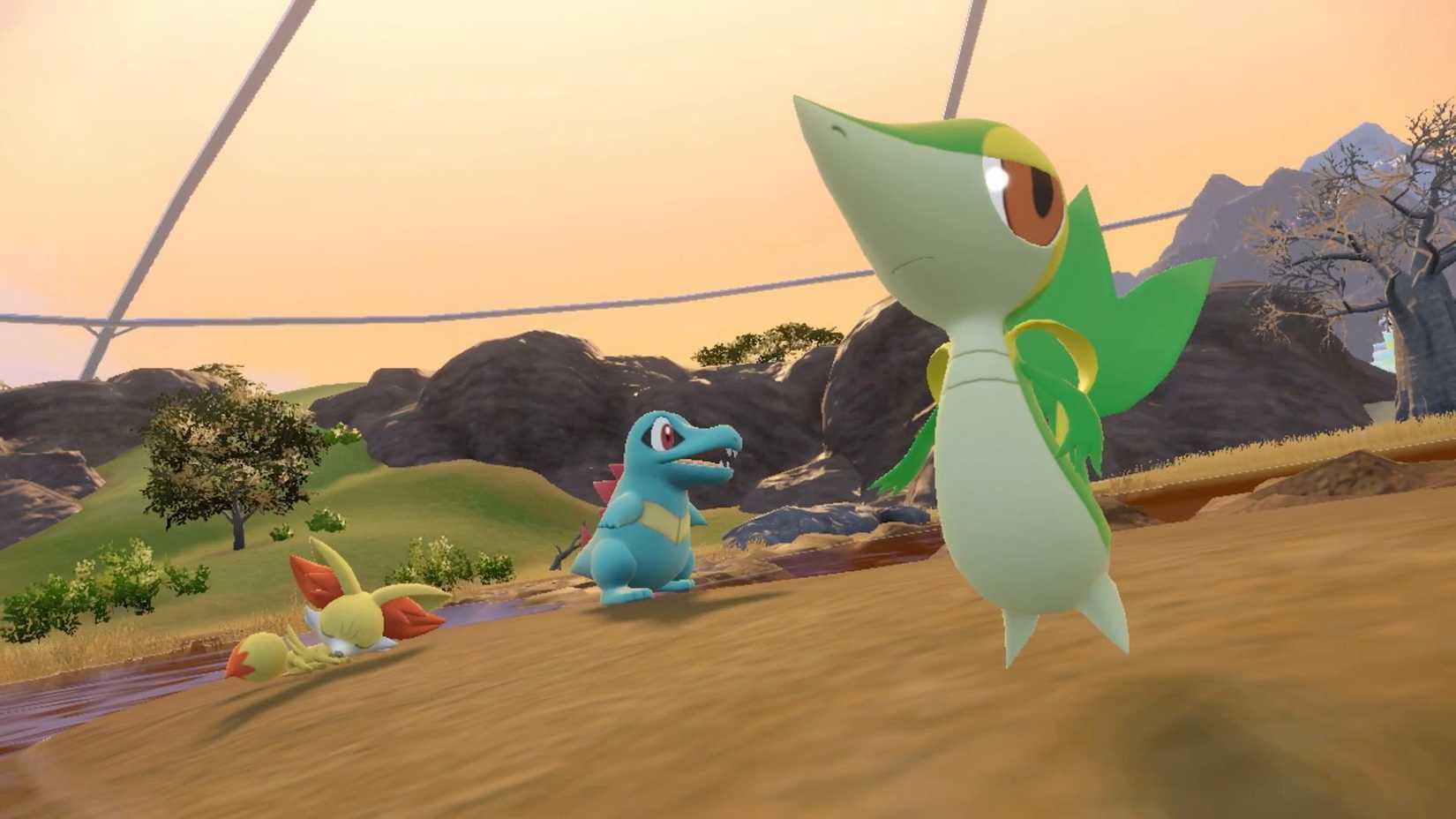 Totodile, Snivy, and Fennekin in Pokémon Scarlet and Violet DLC. They are all hanging out on a grassy field.