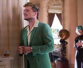 Josh Hutcherson, wearing a green suit and looking like the kind of guy you definitely do not want to take home to meet your parents, smiles by some drinks in The Beekeeper