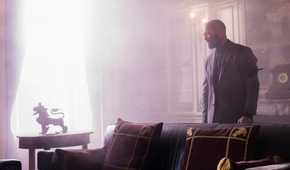 Jason Statham smolders in a brightly lit room with fancy furniture and decorations in The Beekeeper.