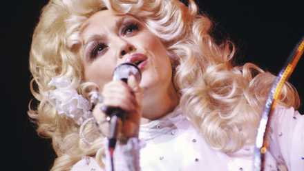 Dolly Parton performs at Georgia Tech Coliseum, Atlanta, in 1977. She’s wearing pink and has a huge blonde hairdo