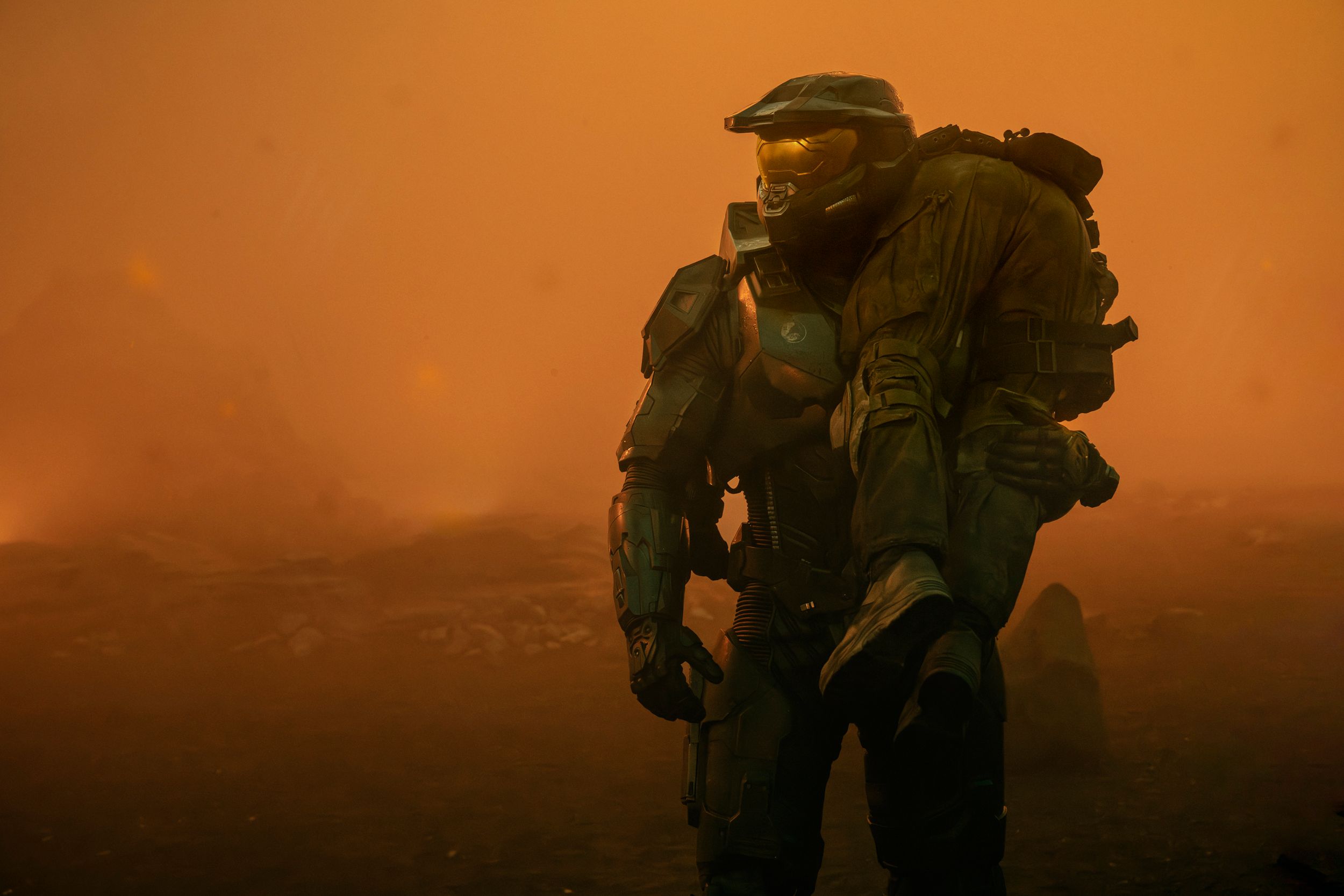 Master Chief (Pablo Schreiber) standing and holding a person slung over his shoulder
