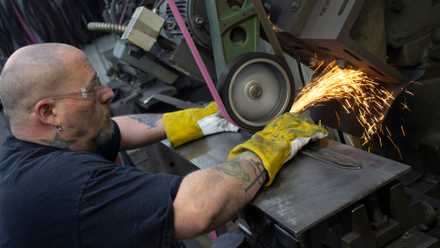 A worker at Sabersmith sharpens a claymore.
