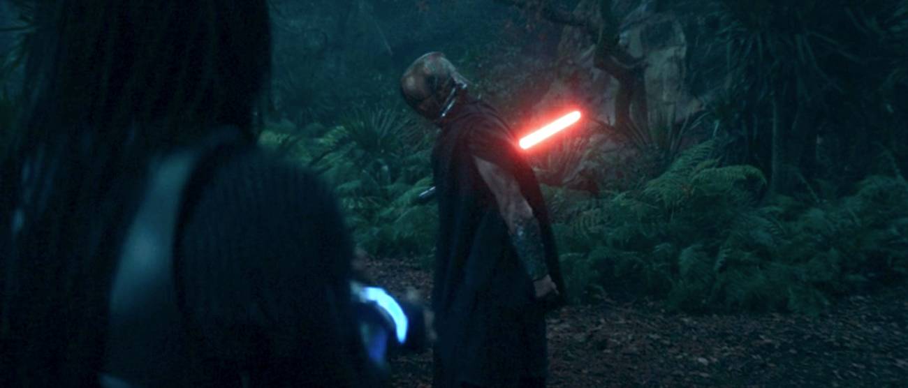 The Master (Manny Jacinto) flexes his muscles as he holds a red lightsaber behind him, preparing to strike Mae in The Acolyte