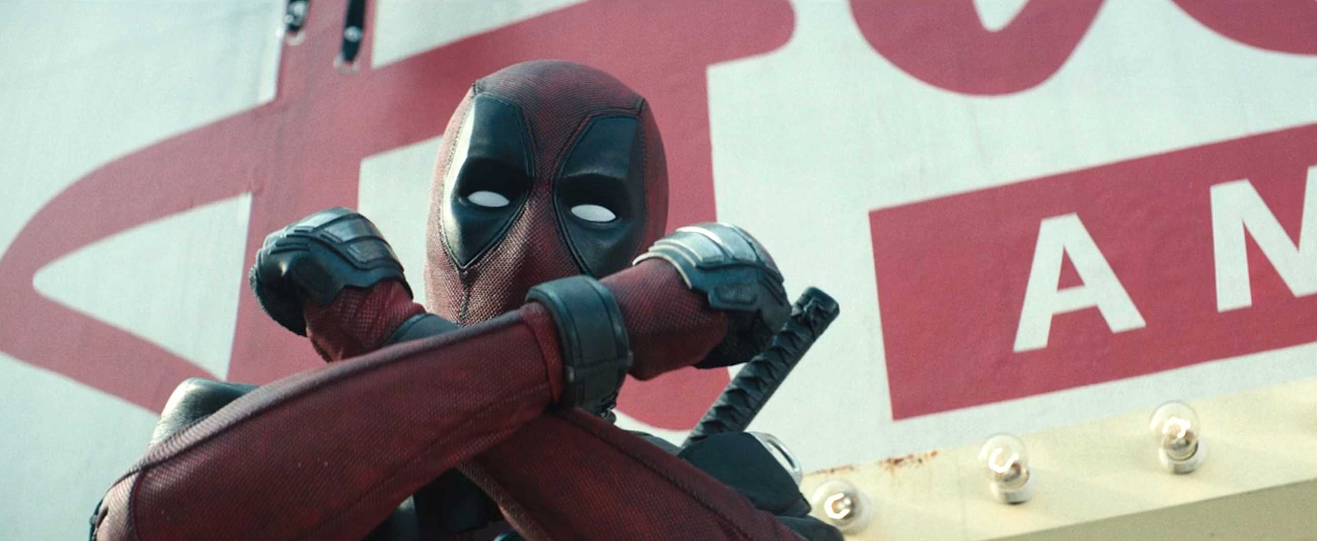 Deadpool (Ryan Reynolds, in costume) stands on a billboard catwalk, making the X-Force crossed-wrists gesture in Deadpool 2
