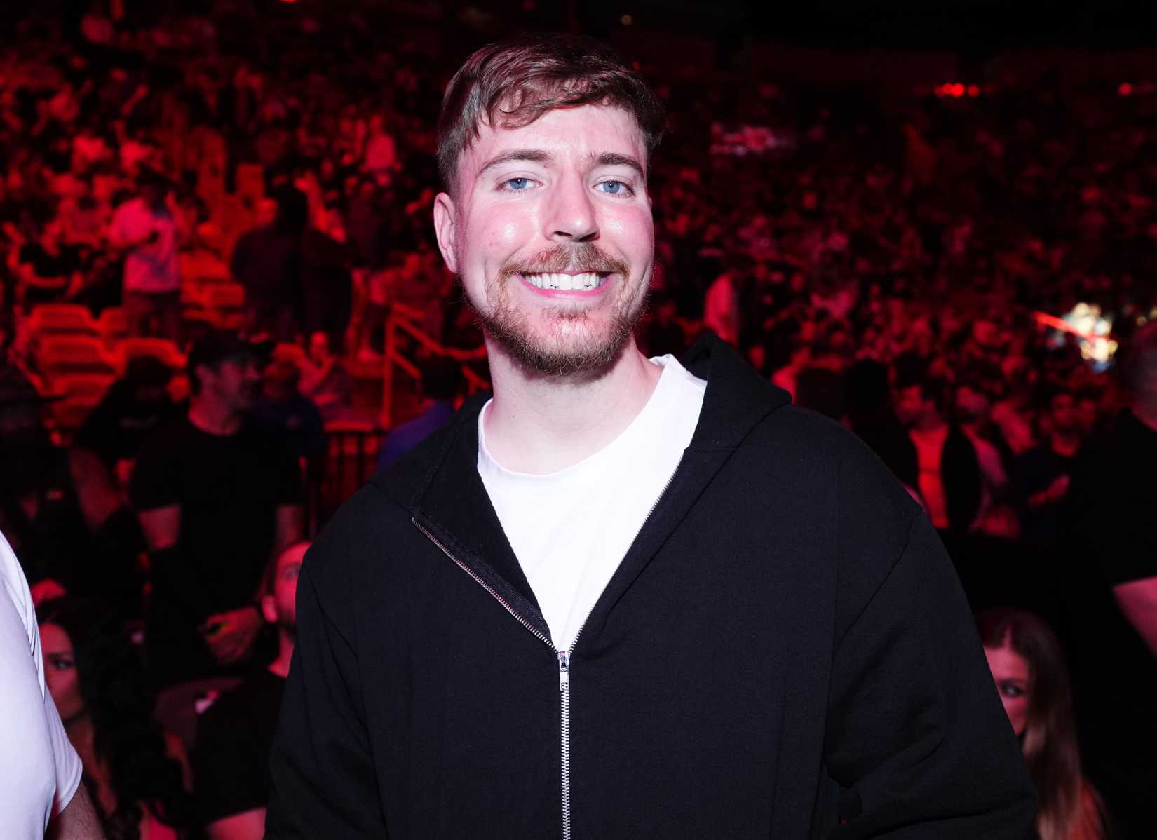A photograph of Jimmy Donaldson, aka MrBeast, smiling at the camera. A huge crowd of people is behind him