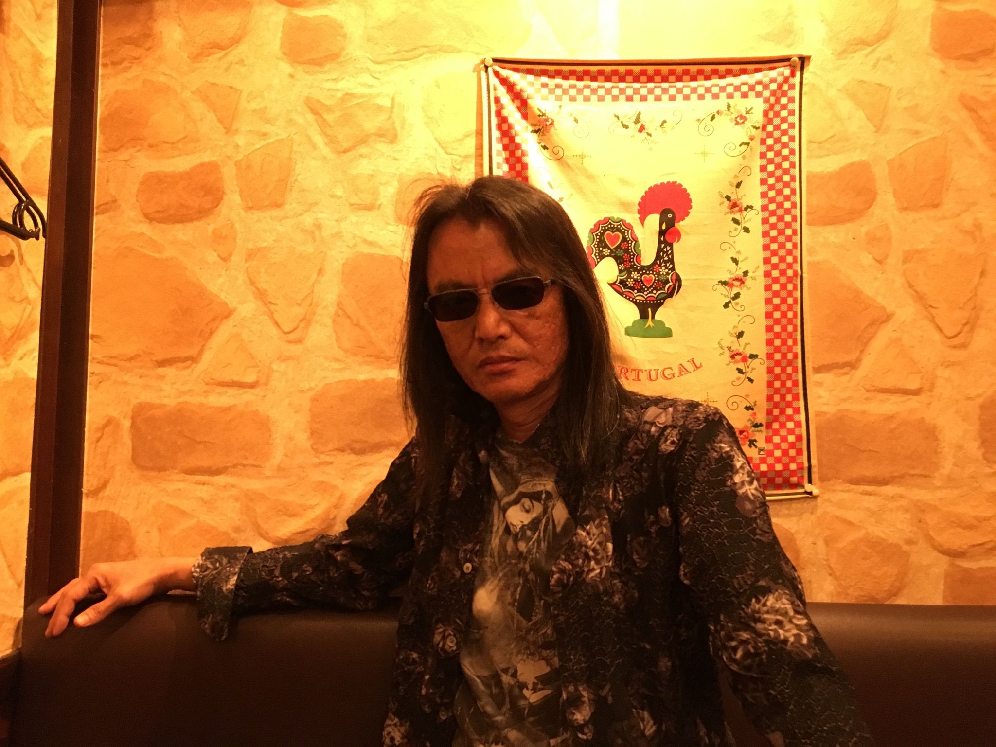 Tomonobu Itagaki, with long hair and sunglasses, in a print shirt